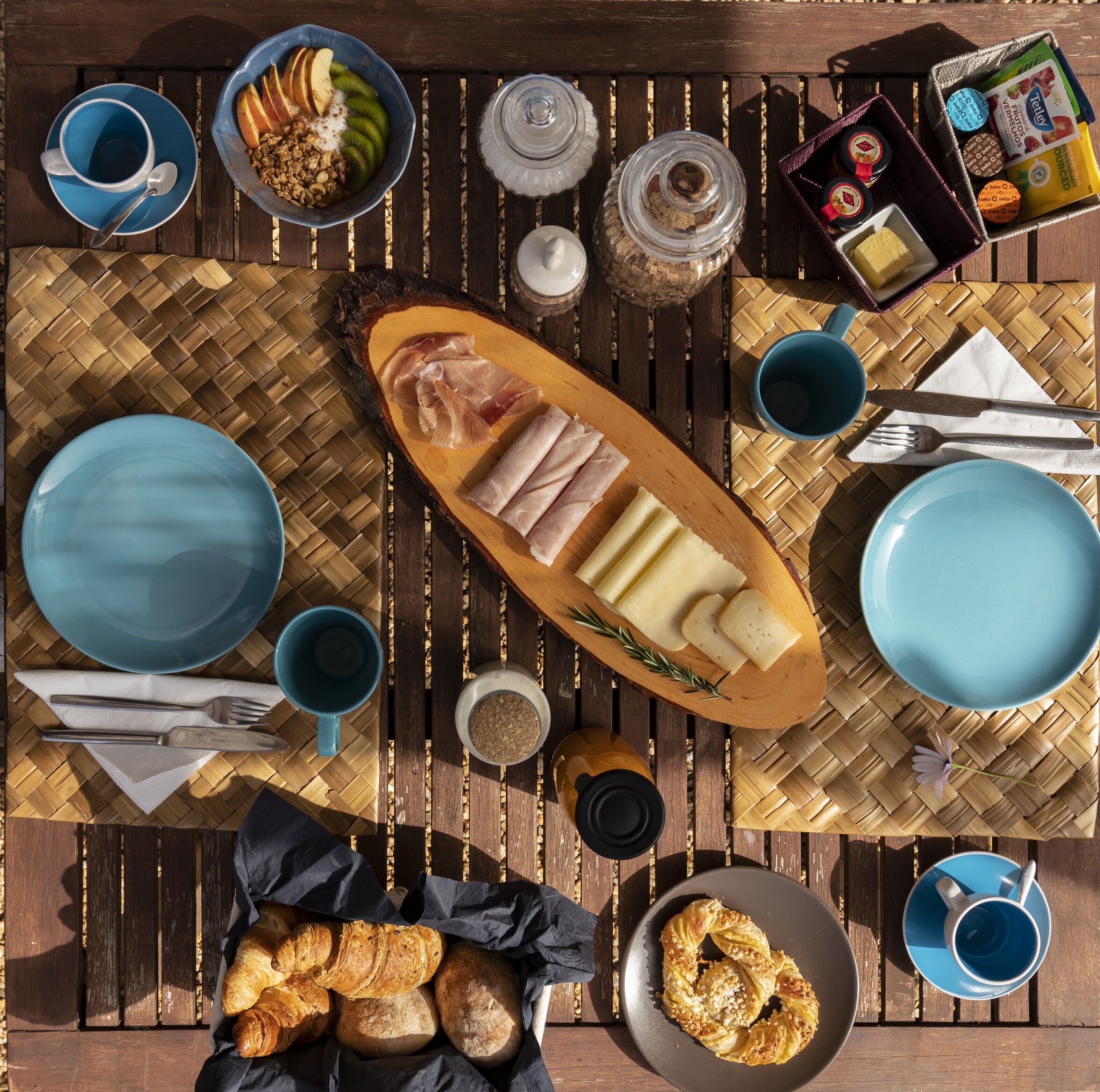 Mesa de café da manhã com pratos, xícaras, tábua de queijos e doces.