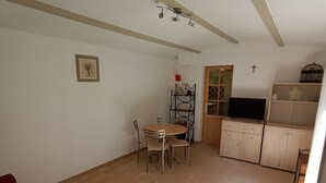 A spacious living area with a red sofa, a dining table with chairs, a TV, and wooden cabinets. - La Chenaie (Mazan)