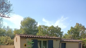 A small house with a tiled roof, a covered patio, and a garden with various plants and flowers. - La Chenaie (Mazan)