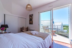 Une chambre avec un grand lit, une table de chevet avec une lampe et des fleurs, un fauteuil et un balcon avec vue.