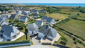 Un quartier résidentiel avec des maisons, un ciel dégagé et une côte visible à l’arrière-plan.