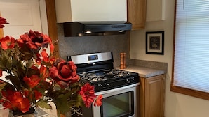 A kitchen with a gas stove, oven, granite countertop, wooden cabinets, and a vase with red flowers.