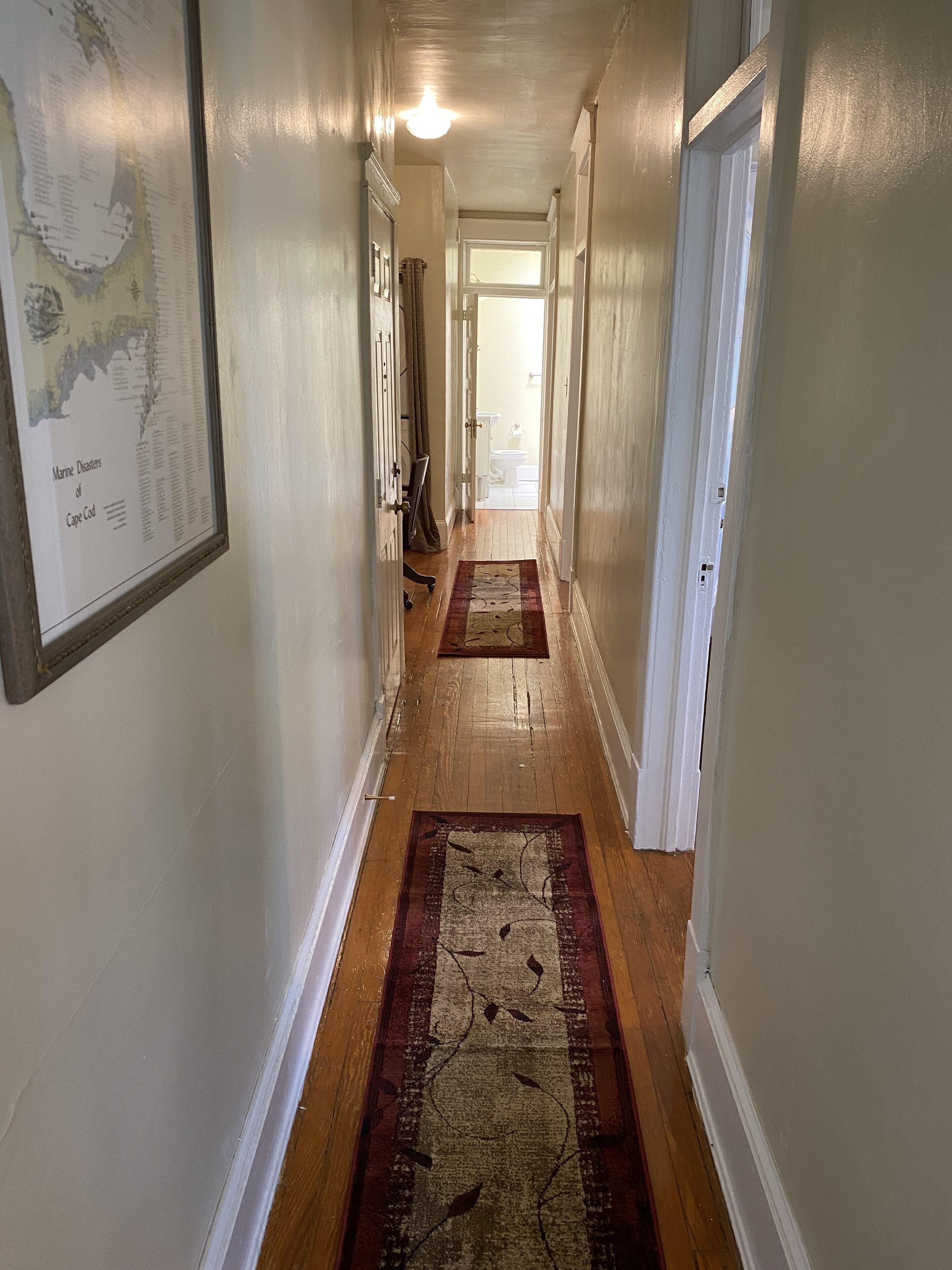 A hallway with wooden flooring, white walls, and a framed map on the left.
