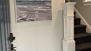 Eine Treppe mit dunklem Teppich und weißen Spindeln, die zu einer Plattform mit einem Bild einer Strandlandschaft führt.