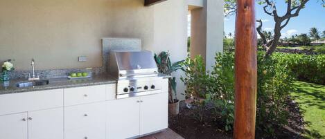 Cocina exterior con una parrilla de acero inoxidable, un lavamanos y una encimera.
