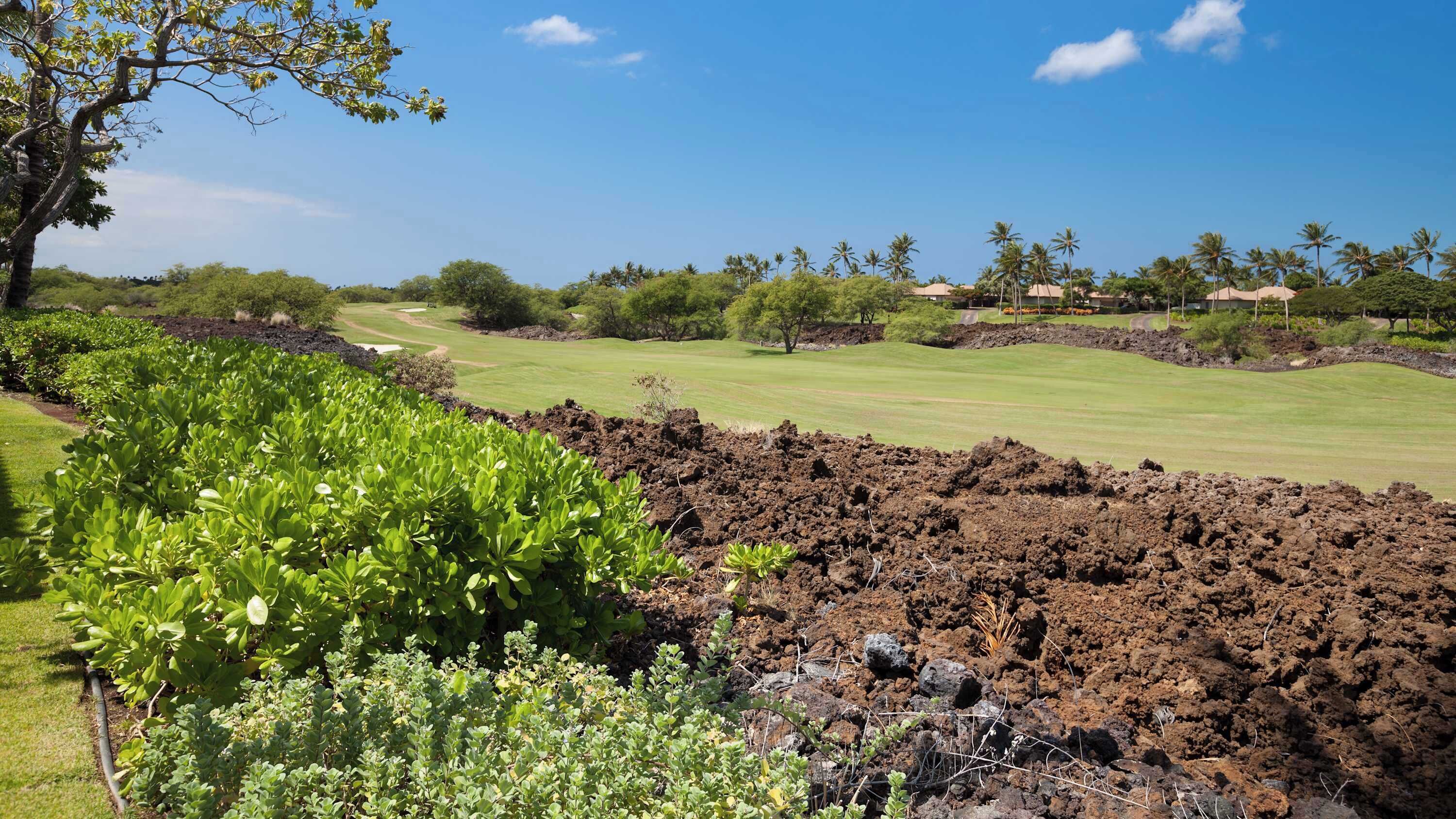 A golf course with a well-maintained green, a rocky area in the foreground, and a clear blue sky.