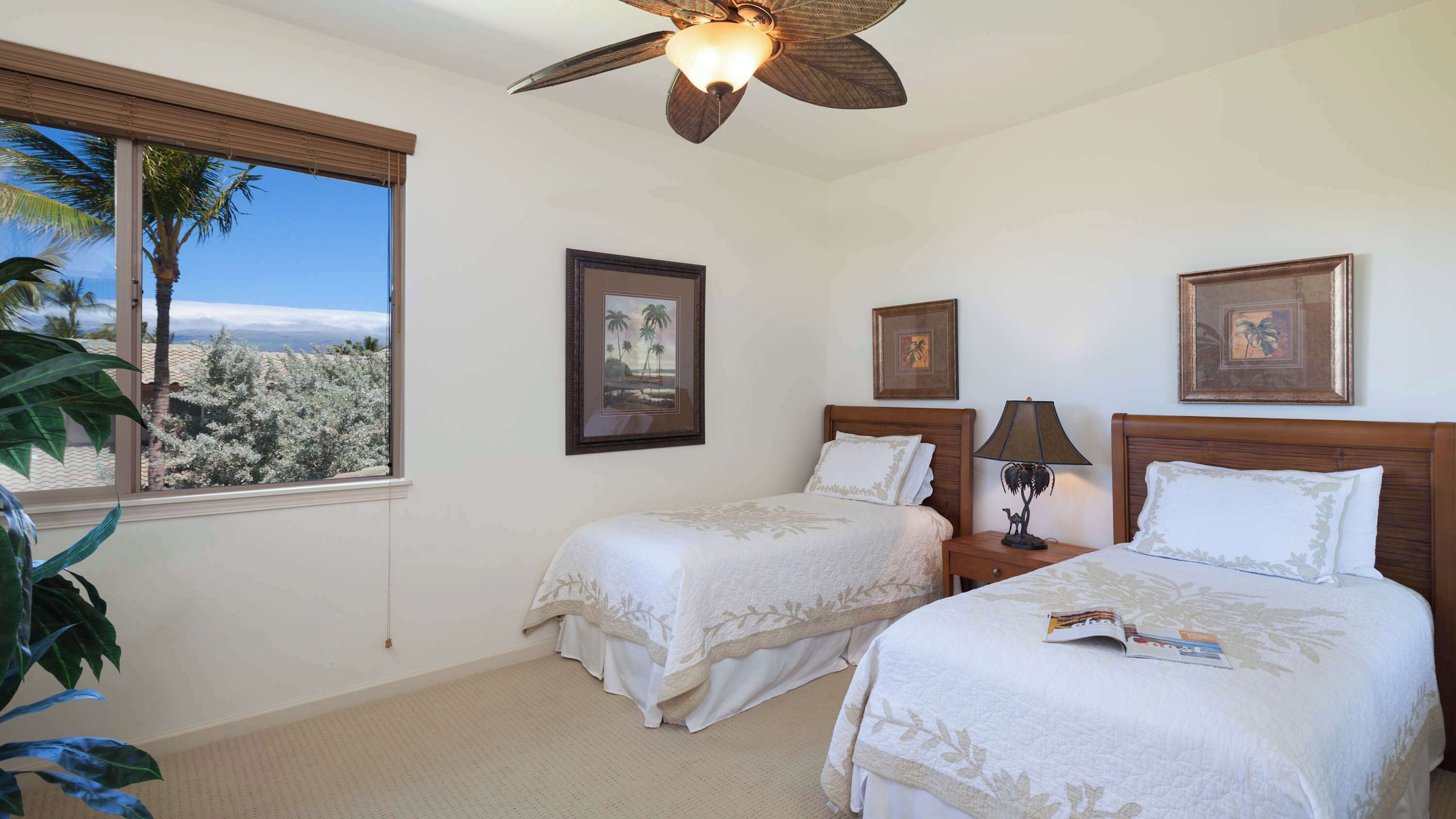 A hotel room with two beds, a ceiling fan, and framed pictures on the wall.