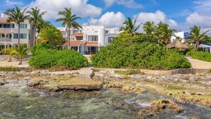 A beachfront hotel with clear waters, palm trees, and a thatched-roof structure. - Stunning 5BR Balam Ek Villa – Oceanfront, Pool & Exceptional Views (Akumal)