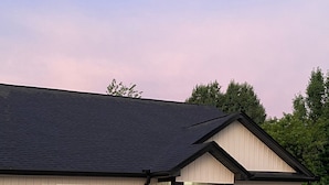 A single-story house with a dark roof, beige siding, and black shutters.