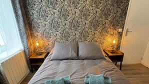 A neatly made bed with two pillows and folded towels in a room with patterned wallpaper and bedside lamps. - Apartment with terrace and private parking in Concarneau, Brittany (Concarneau)