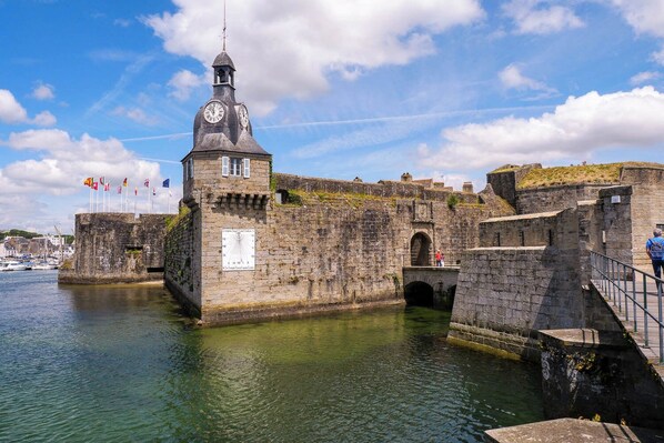 A historic stone building with a clock tower, situated by a body of water, featuring a stone bridge and flags. - Apartment with a terrace and private parking in Concarneau, Brittany (Concarneau)