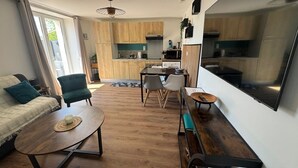 A modern living room with a sofa, coffee table, and chairs. A kitchen is visible in the background with wooden cabinets and a dining area. - Apartment with terrace and private parking in Concarneau, Brittany (Concarneau)