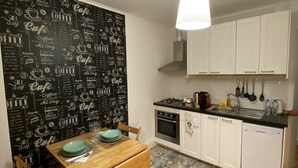 Eine kleine Küche mit weißen Schränken, einem Holztisch und einer Wand mit Kaffee-Bezug.