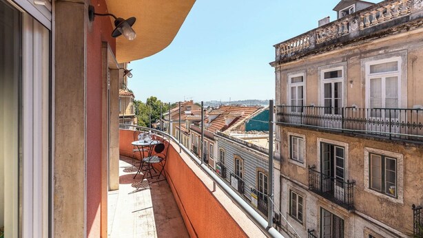 Ein Balkon mit Tisch und Stühlen, mit Blick auf eine Stadtlandschaft mit historischen Gebäuden.