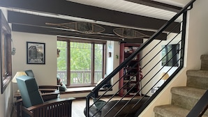 Un salon avec un banc en bois, un canapé, un escalier doté de rampes noires et une bibliothèque.