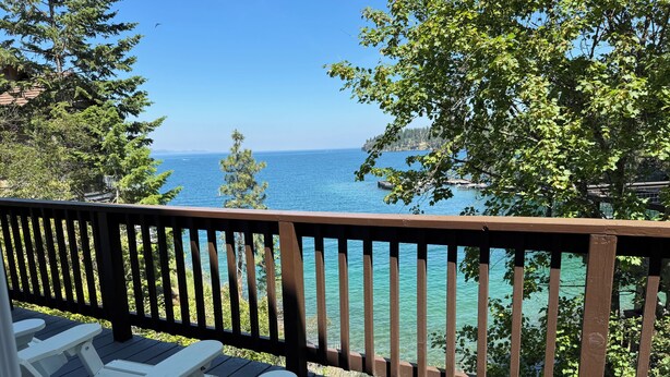 Une terrasse en bois avec des fauteuils Adirondack blancs donnant sur une mer d’un bleu limpide.