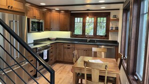 Une cuisine moderne dotée de meubles en bois, d’appareils électroménagers en acier inoxydable et d’un coin repas avec une table et des chaises en bois.