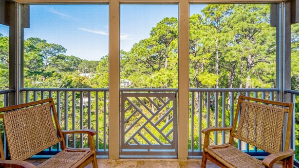 A balcony with two wicker chairs, a lattice screen, and a view of a forested area. - Completely Renovated Condo- Top Floor w/ Elevator.  8 Min walk to the Beach! (Santa Rosa Beach)