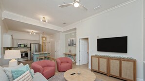 A modern living room with a round coffee table, red armchairs, a flat-screen TV, and a kitchen in the background. - Completely Renovated Condo- Top Floor w/ Elevator.  8 Min walk to the Beach! (Santa Rosa Beach)