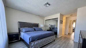 A bedroom with a large bed, a nightstand, a dresser, and a mirror. - Cheerful 3-Bedroom home w/ Pool(minutes to the Strip) (Las Vegas)