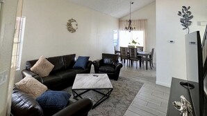 A modern living room with a black leather sofa, a marble coffee table, and a dining area in the background. - Cheerful 3-Bedroom home w/ Pool(minutes to the Strip) (Las Vegas)