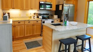 A modern kitchen with wooden cabinets, stainless steel appliances, a granite countertop, and a window providing natural light. - Rock Pond Condo 53 - Ski in Ski out Rock Pond Condo at Saddleback (Rangeley)