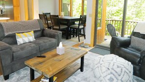 A cozy living room with a sofa, coffee table, and a dining area with chairs and a table. - Rock Pond Condo 53 - Ski in Ski out Rock Pond Condo at Saddleback (Rangeley)