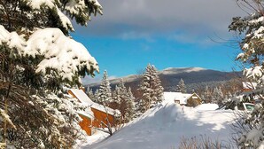 A snow-covered road with houses on either side, a clear sky, and a mountain in the background. - Rock Pond Condo 53 - Ski in Ski out Rock Pond Condo at Saddleback (Rangeley)
