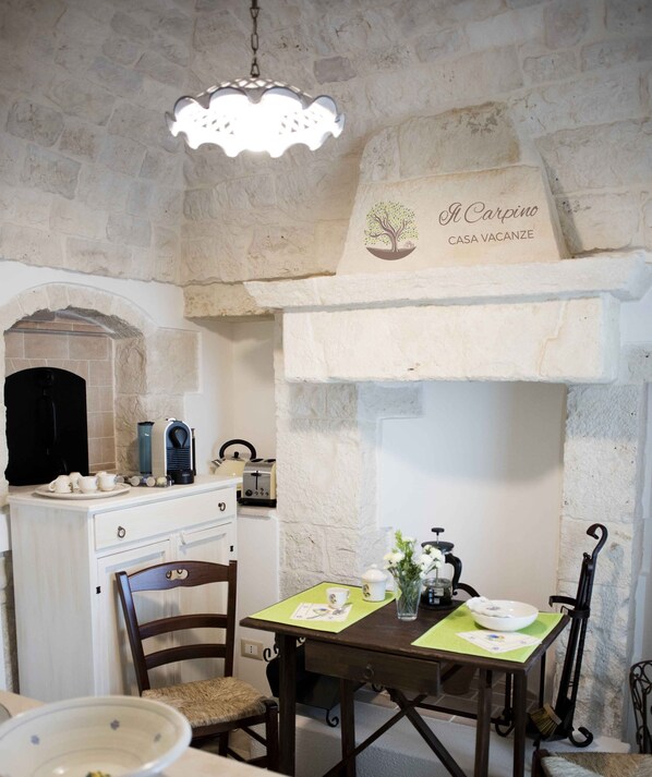 Une pièce rustique aux murs de pierre, dotée d’une cheminée, d’une table à manger avec des chaises et d’un coin café.