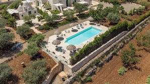 Vista aérea de una villa con piscina, arquitectura de piedra y vegetación circundante.