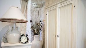 Una lámpara de cerámica blanca, un florero de cerámica blanca con flores secas y un mueble blanco con dos tiradores.