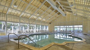 Ein Innenpool mit klaren Glaswänden, einer hohen Decke mit Gittermustern und mehreren Liegestühlen rund um den Pool.