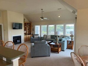 A spacious living room with a fireplace, a television mounted on the wall, and a large window providing natural light.