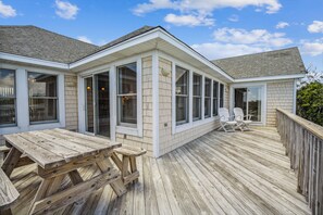 A covered deck with a wooden table and chairs, large windows, and a brick exterior wall. - DUCK-20 "DUCK On Inn"   Sun to Sun  Pet-Friendly! Oceanside (Duck)