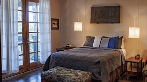 Een slaapkamer met een groot bed, twee nachtkastjes, een bankje en een raam met gordijnen.