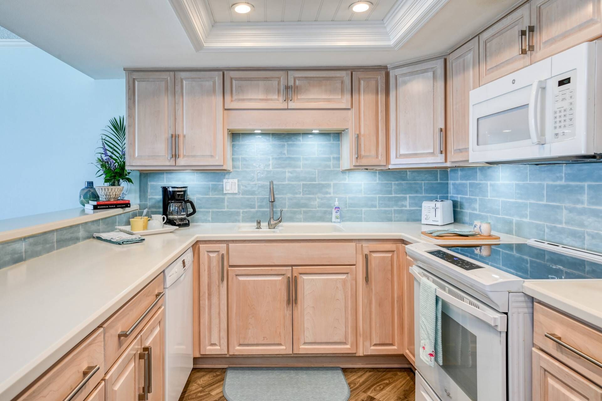 A modern kitchen with light wood cabinets, a white countertop, a built-in microwave, and a stainless steel oven.
