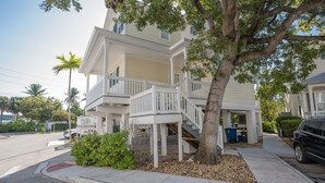 Une maison à deux étages avec un balcon, un arbre devant et une voiture garée.