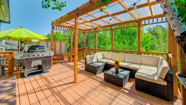 A covered outdoor patio with a grill, seating area, and a pergola with a glass roof.