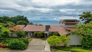 A modern house with a tiled roof, surrounded by lush greenery and a view of the sea. - Looking for a paradise destination? Casa Tres Monos is ready to welcome you. (Peninsula Papagayo)