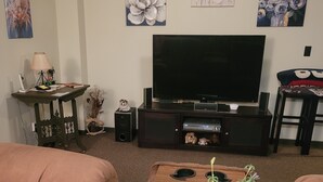 Een woonkamer met een flatscreen-televisie, twee banken, een bijzettafel met een decoratieve plant en wanddecoratie.