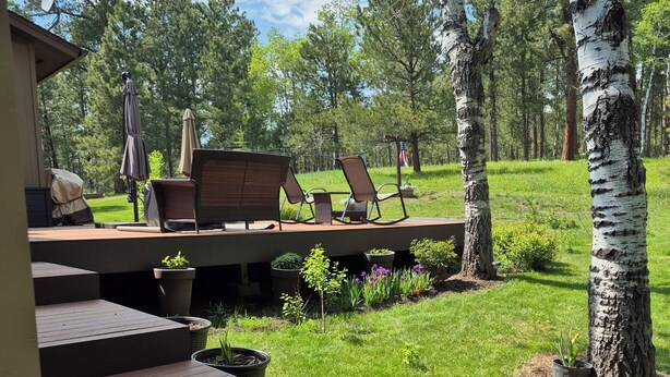 Een houten terras met tuinmeubilair, een kleine tuin met potplanten en uitzicht op een bebost gebied.