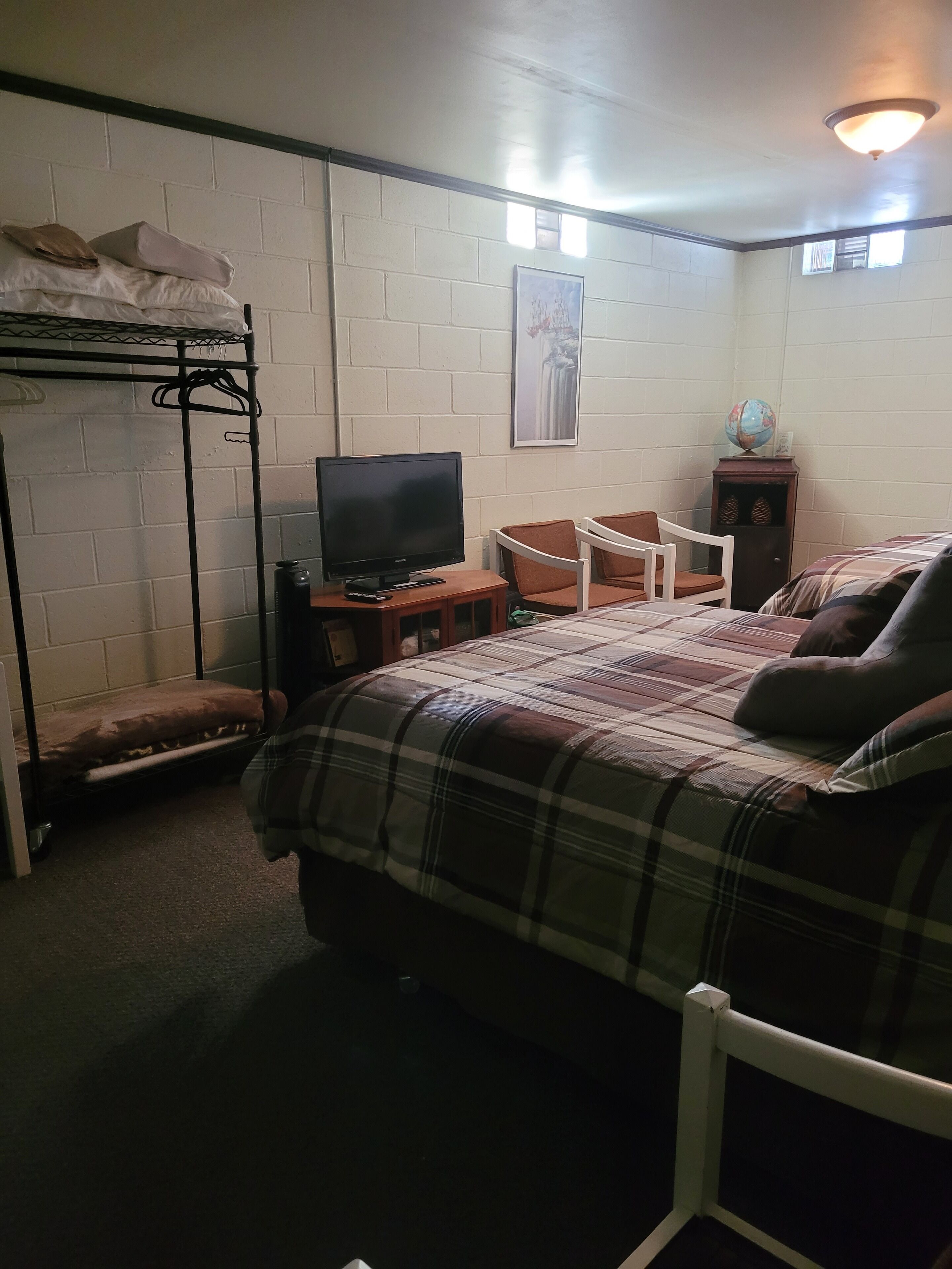 Un dormitorio con una cama litera, un escritorio con televisor, una silla, un globo terráqueo y un cuadro en la pared.