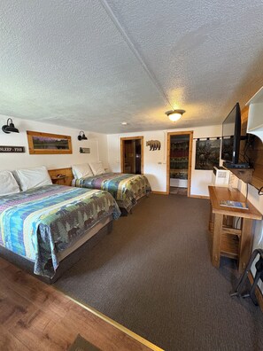 A room with two beds, a desk, a television, and a door leading to another room.