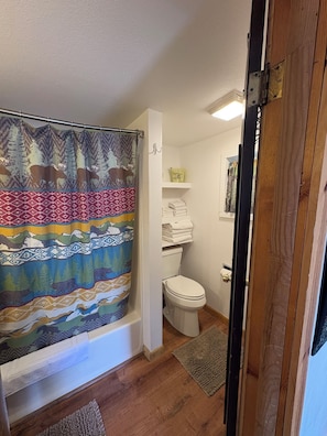 A bathroom with a shower curtain, a toilet, a shelf with towels, and a rug.