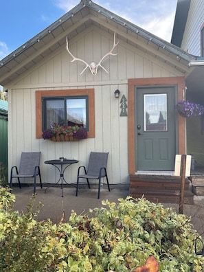 A building with a gray door, a window with a flower box, and two chairs outside.