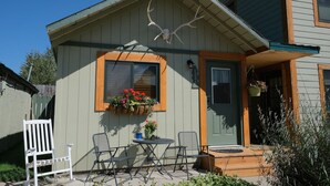 Ein kleines Haus mit einer Veranda, einem hölzernen Schaukelstuhl, einem Tisch und einem Blumenkasten mit roten Blüten.