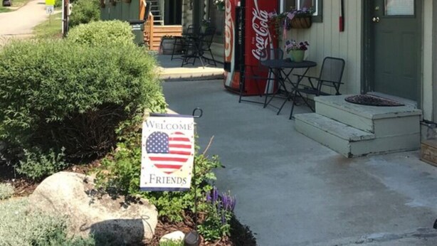 Ein zweistöckiges Gebäude mit grüner Dachbegrünung, einem Coca-Cola-Schild, Außenplätzen und einem Willkommensschild mit einer amerikanischen Flagge.