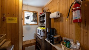 Eine kompakte Küche mit Mikrowelle, Toaster und Kaffeemaschine. Ein Feuerlöscher ist an der Wand angebracht, und ein Schild mit der Information über eine Reinigungsgebühr ist sichtbar.