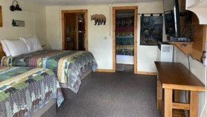 Ein Schlafzimmer mit zwei Betten, einem Schreibtisch, einem Fernseher und einer Tür zu einem anderen Raum.