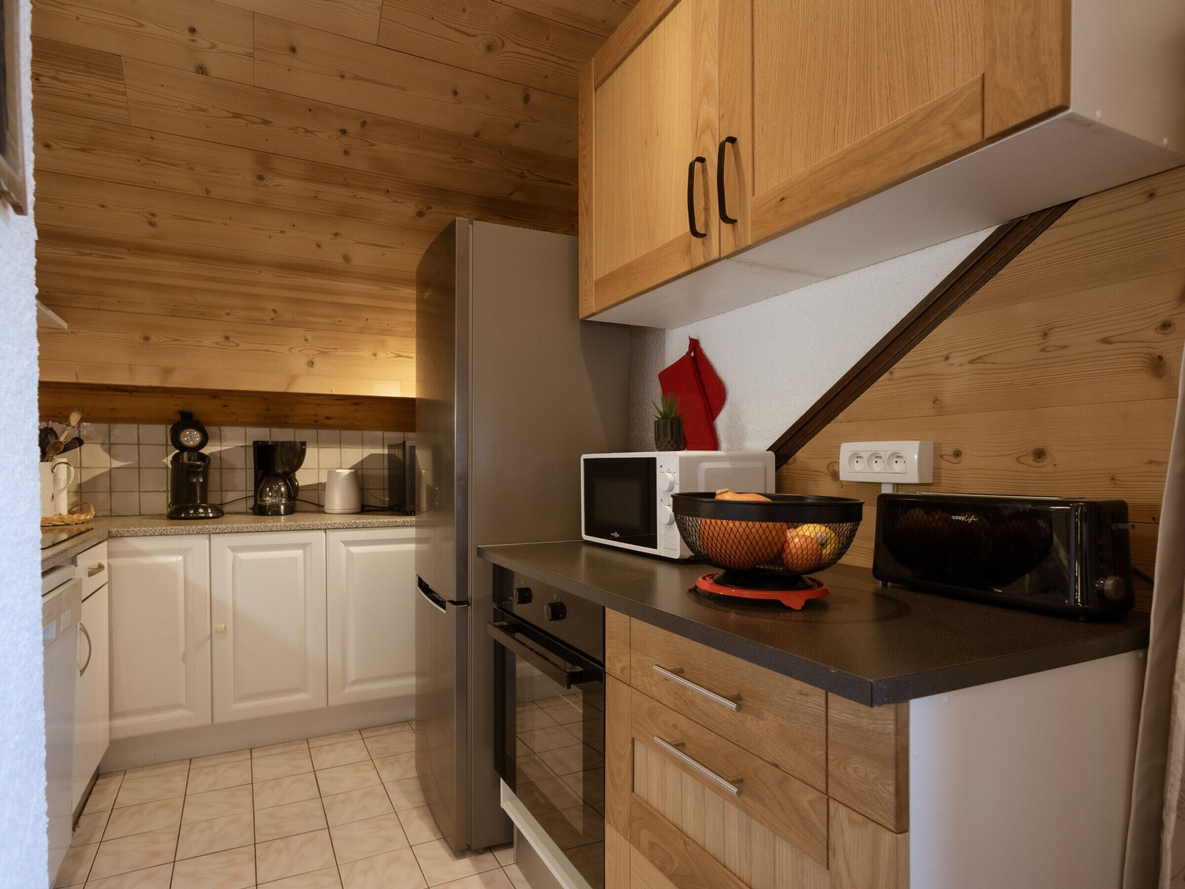 Eine Küche mit Holzausstattung, einem Edelstahlkühlschrank, einer Mikrowelle und einem Toaster.